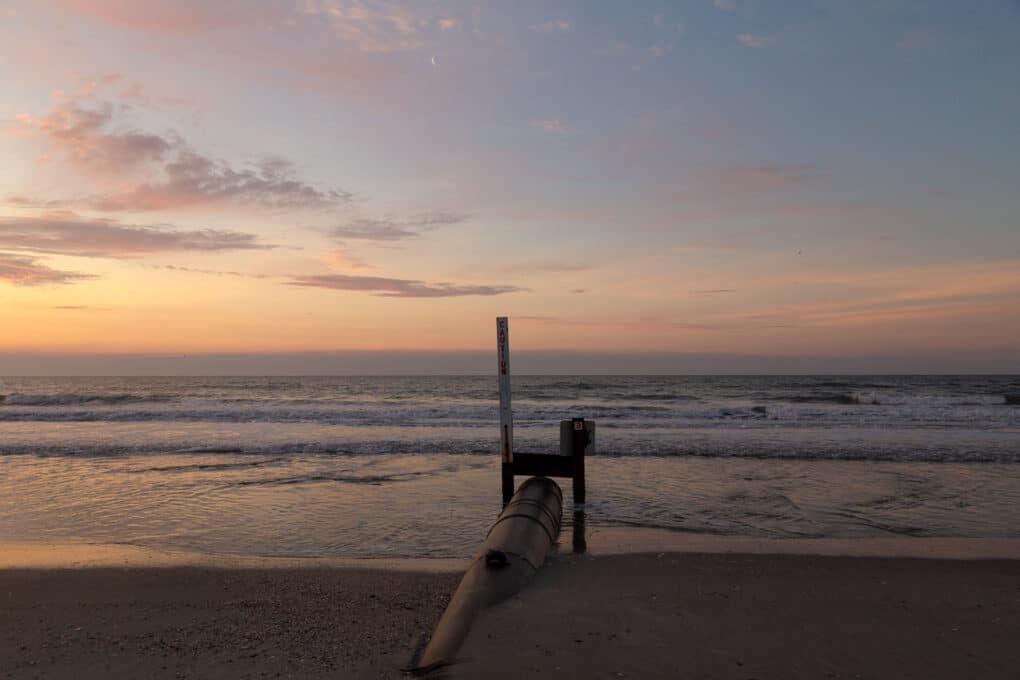 Color photograph of pink sky over the ocean.