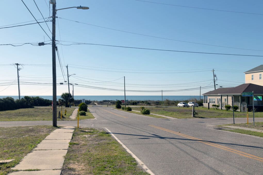 Color photograph of quiet street with small houses, leading to the beach and the ocean.