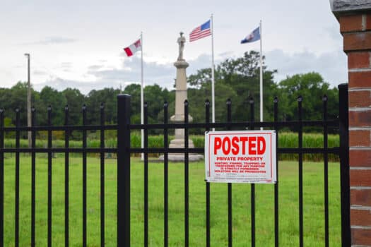 Color photograph of a Civil War statue, situated in a grassy space behind a wrought-iron fence on which hangs a sign reading POSTED: PRIVATE PROPERTY.