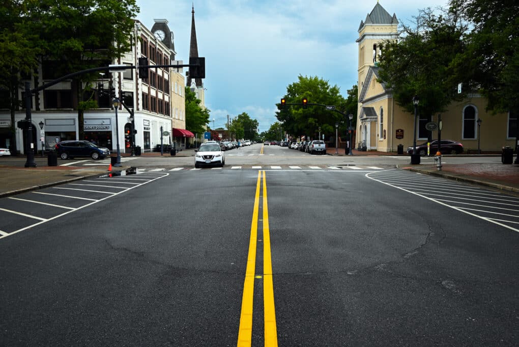 Color photograph of empty intersection in a small town. The outline of a large circle is just visible in the fresh asphalt.