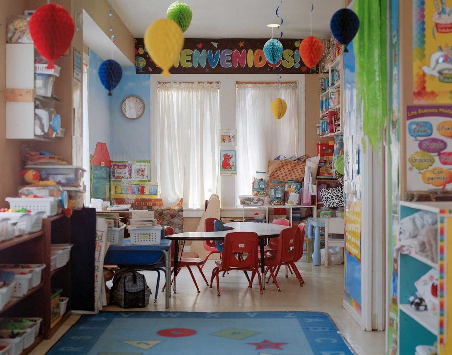 Click to Enlarge Color photograph of interior of nursery school, with rugs, books, little table and chairs, etc.