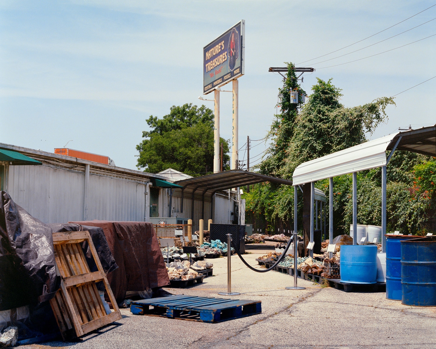 Click to Enlarge Color photograph of outdoor rock shop, with rocks on pallets under awnings.