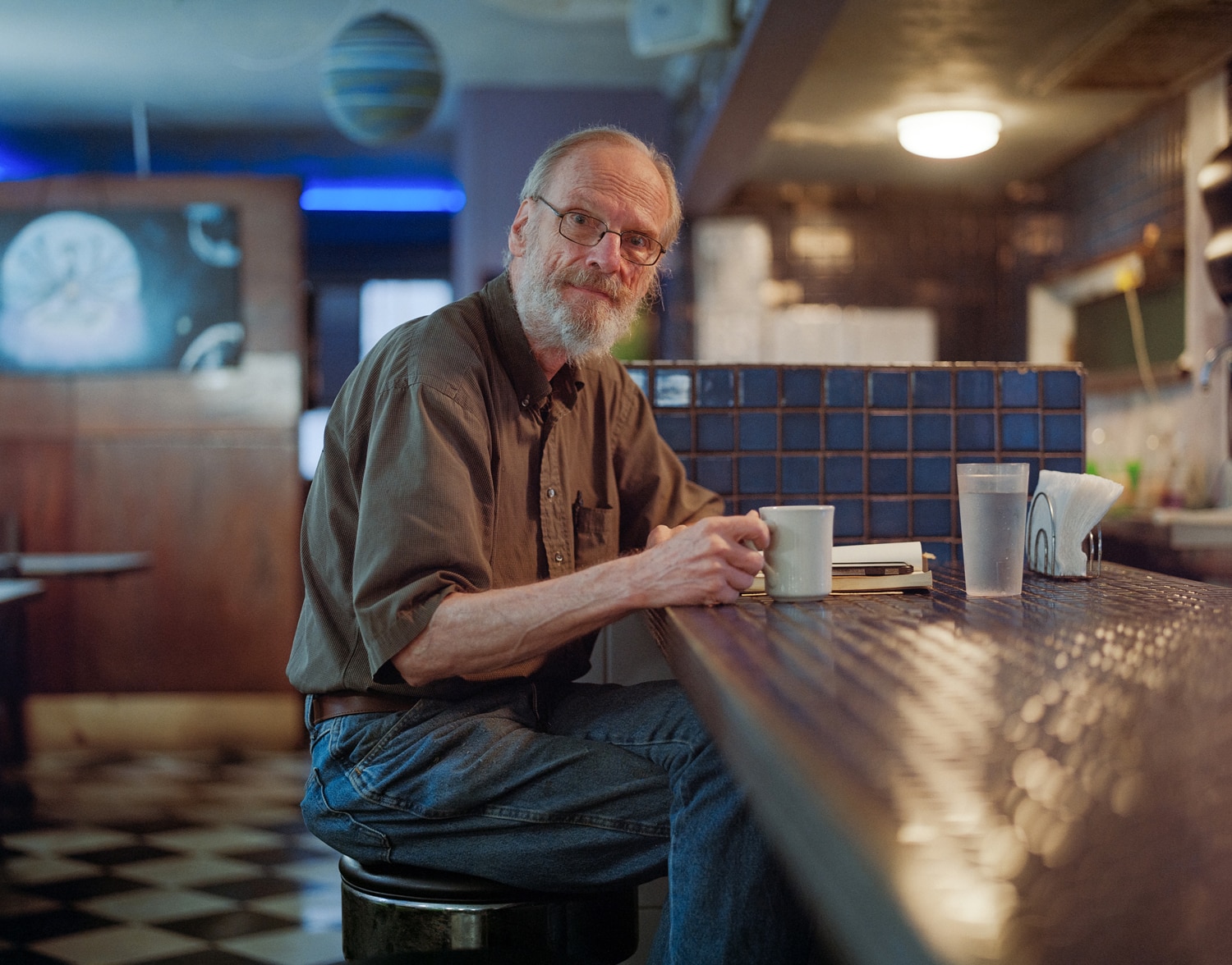 Click to Enlarge Color photograph of middle-aged white man drinking coffee at diner counter.