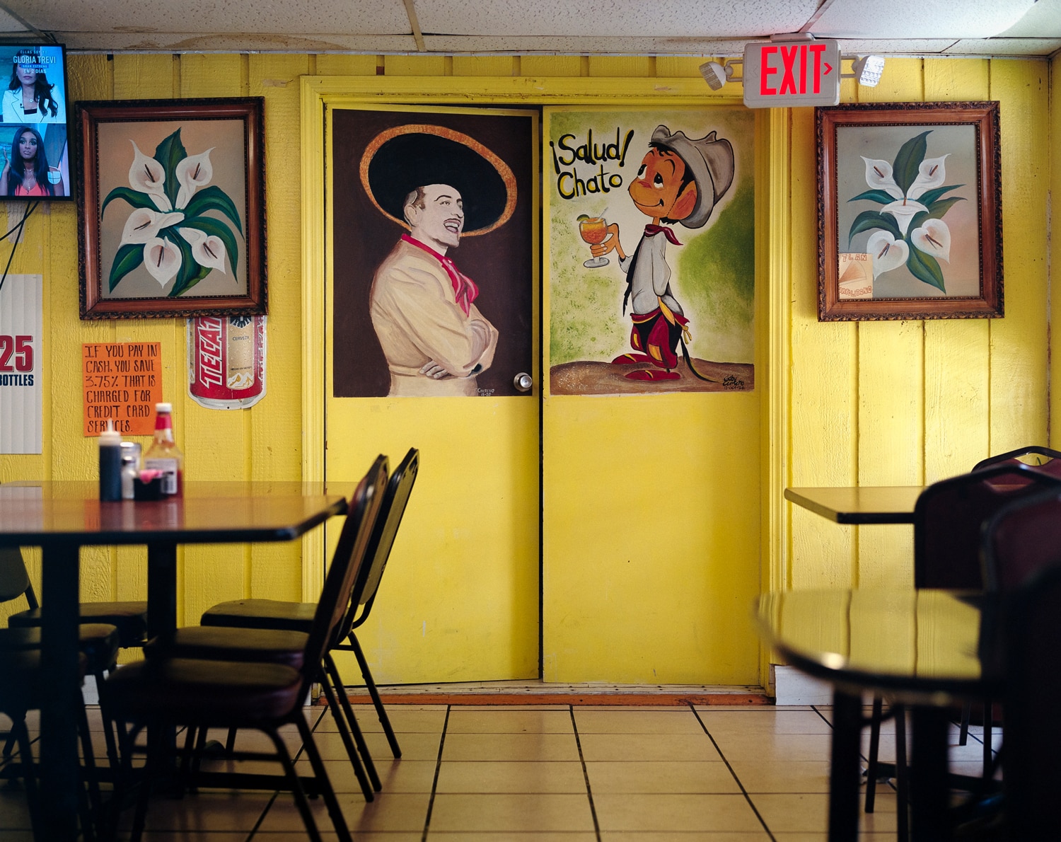 Click to Enlarge Color photograph of a restaurant interior, painted yellow, with signs and pictures on the wall.