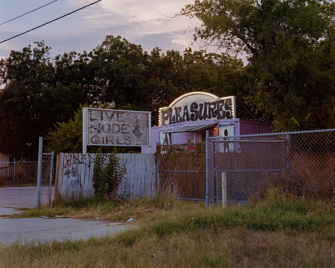 Click to Enlarge Color photograph of a small trailer with signs reading PLEASURES and LIVE NUDE GIRLS.