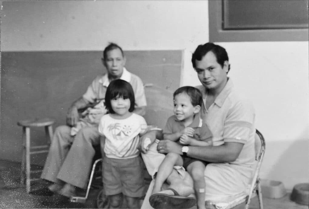BLack-and-white photograph of two small children, a young man, and an older man.