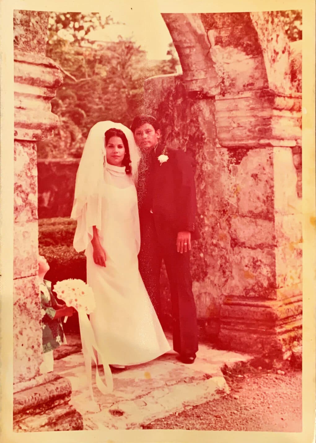 A young couple, she in a bridal dress, he in a suit with a white flower in his buttonhole.