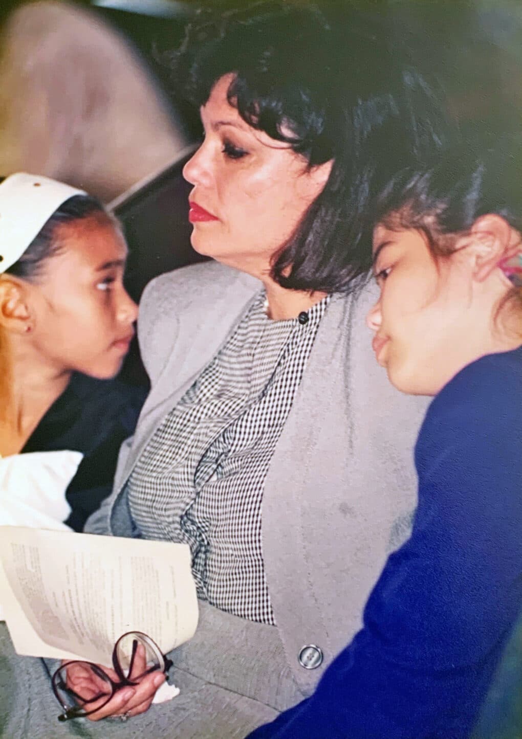 Color photograph of middle-aged Asian woman in a gray suit; beside her, a small girl in a blue dress leans her head on her mother's shoulder.