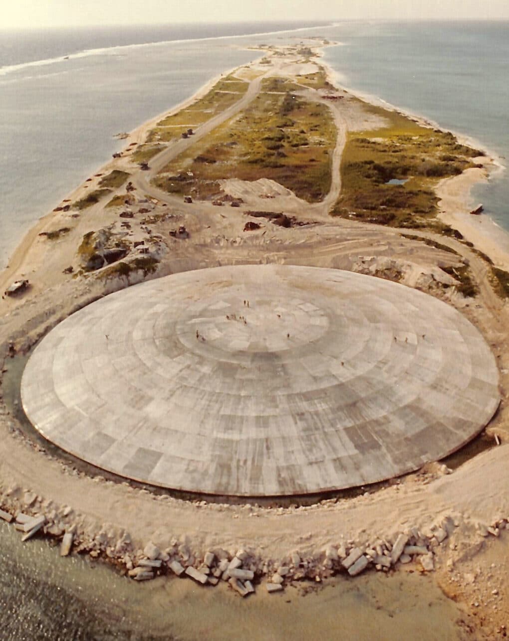 Color aerial photo of an enormous concrete dome on a sandy atoll.