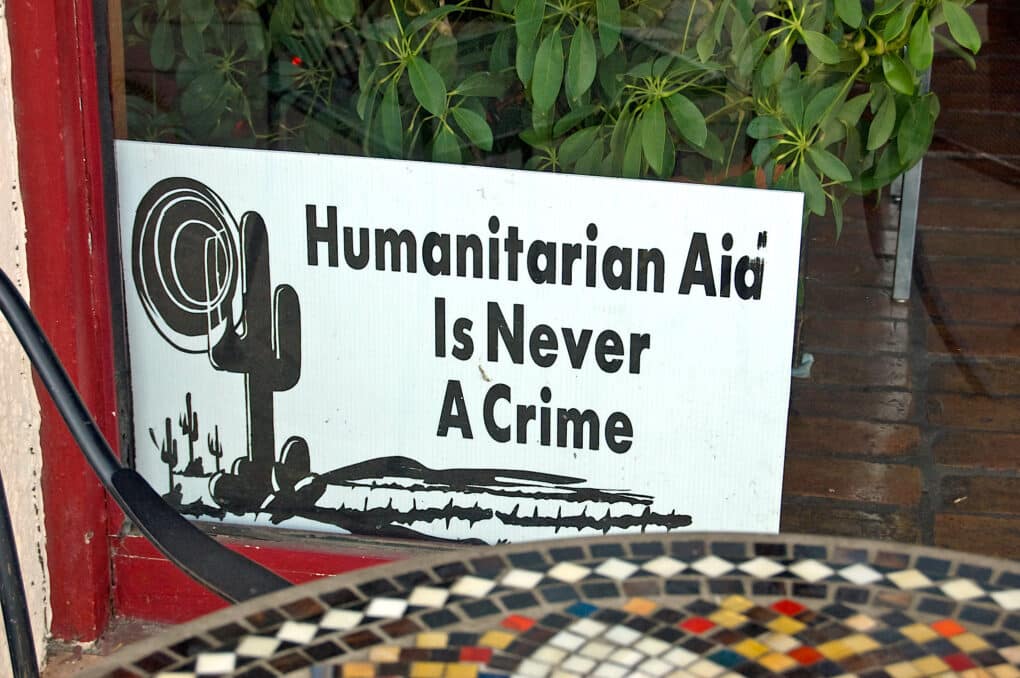 Picture of a sign tucked in corner of a store window; sign says "Humanitarian Aid is Never a Crime."