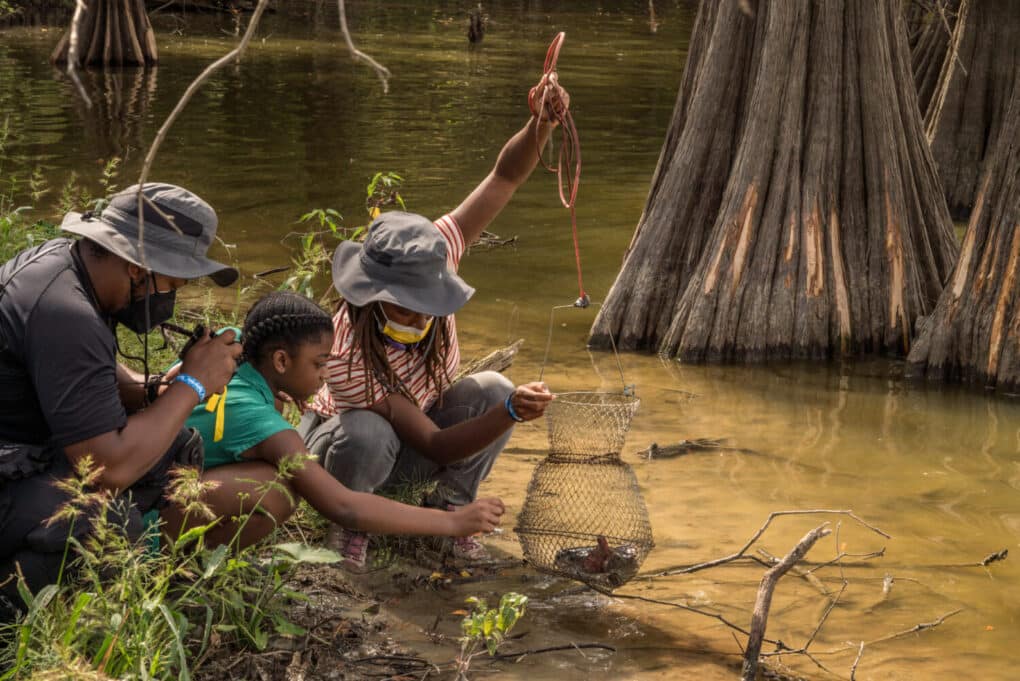 Color production still of cinematographer and director working with child actor beside a river.