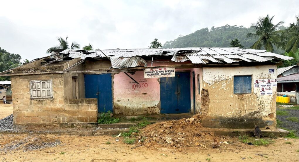 Color photo of very dilapidated building: small, one-story, concrete with metal roof.
