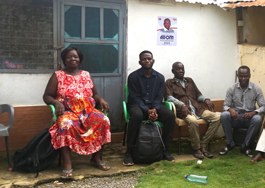 Color photo of four people—three men and one woman—sitting on chairs, looking directly at camera.