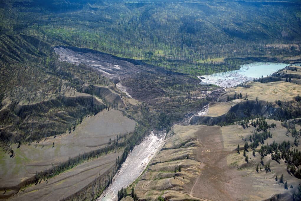 Color aerial photograph of large mudslide blocking course of swift-running river.