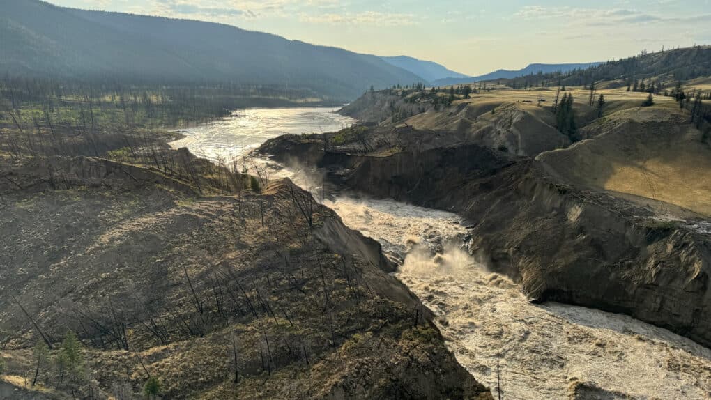 Color photograph of fast-running river with large muddy area beside it.