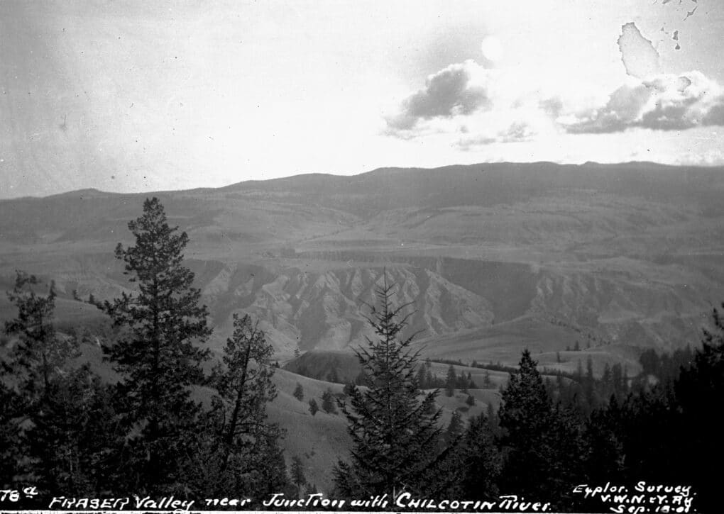 Black-and-white photograph of high rocky cliffs with evergreens in foreground; caption handwritten in white at lower edge.