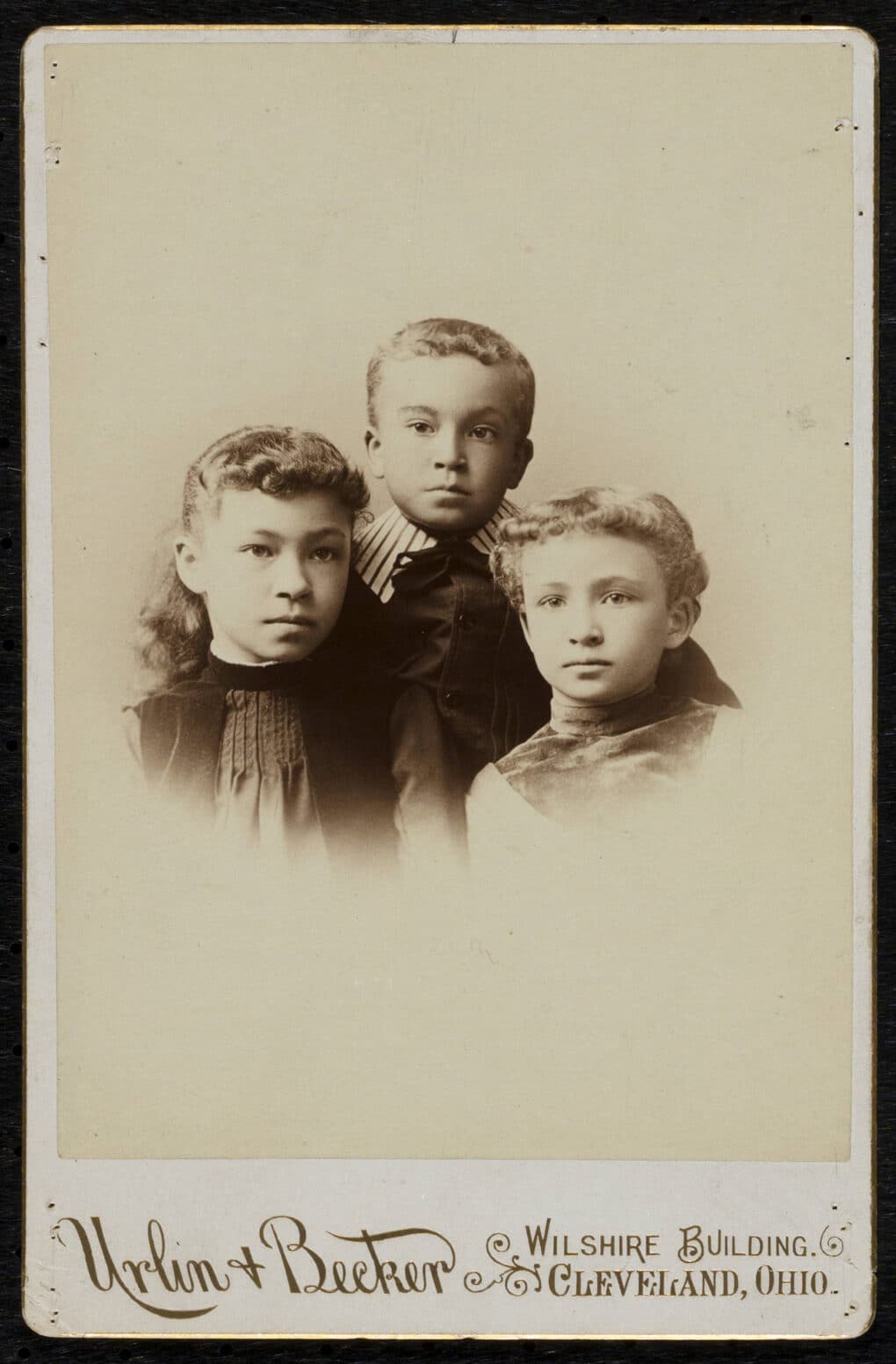 Cabinet photograph of three well-dressed, biracial, late-19th-century children.