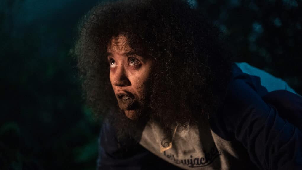 Color film still of light-skinned Black teenager, gazing up in stark light at night, her face covered in dirt.