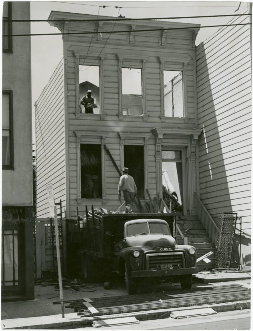 Black-and-white photograph of small Victorian house being torn down.