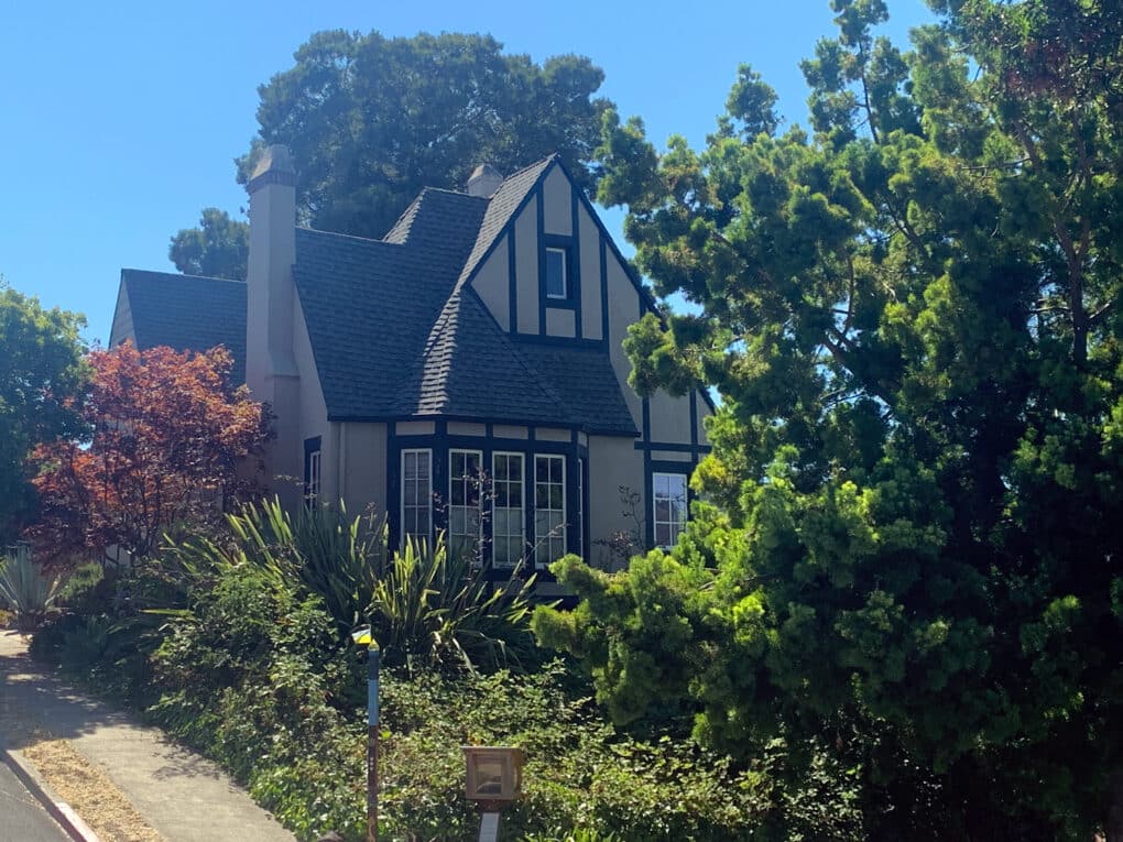 Color photograph of Tudor-style house in lush garden under bright blue sky.