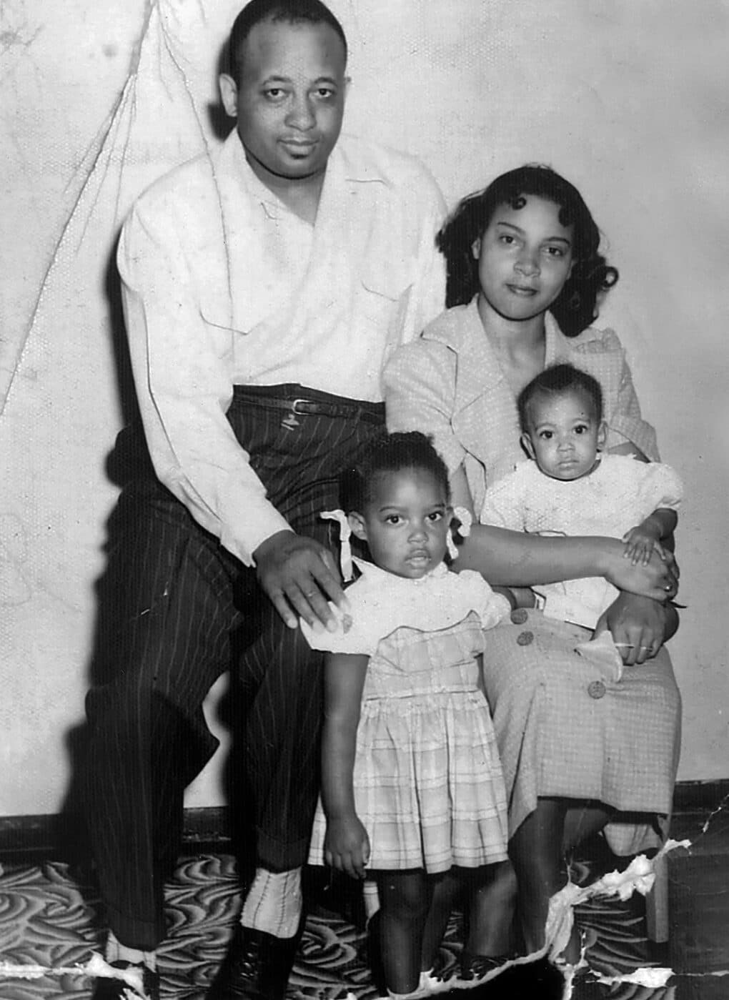 Black-and-white photograph of young Black family with two small children seated for a studio portrait.