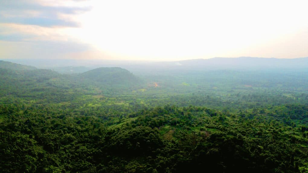 Color landscape photo taken from hill or mountain, showing very green, lush rolling hills with a small mountain and a road visible in the distance.