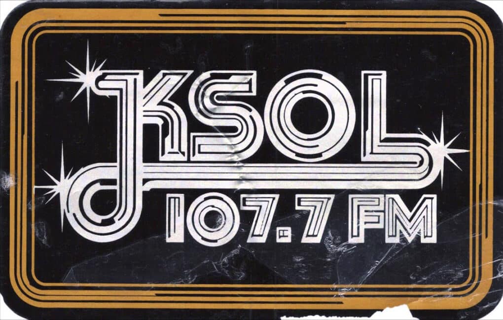 The call letters KSOL and radio-dial address 107.7 FM appear in silver letters on a black background in a brown frame.
