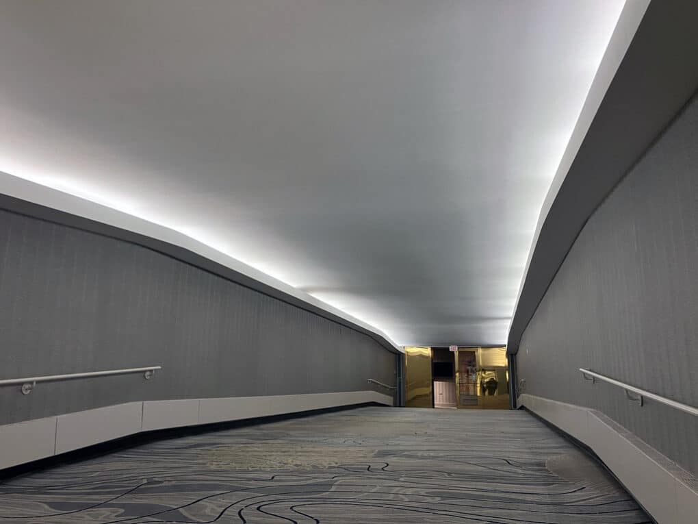 Color photograph of underground passageway with recessed lighting, gray carpeting, and handrails.
