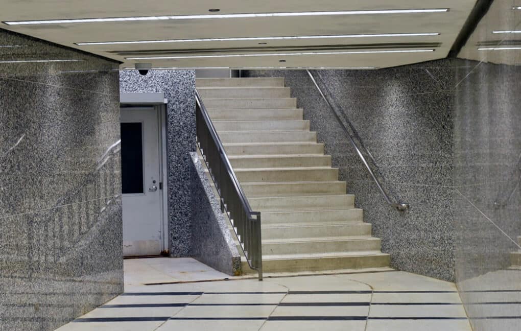 Color photograph of underground corridor sheathed in polished granite, but with dirty floor and awkward dropped ceiling.