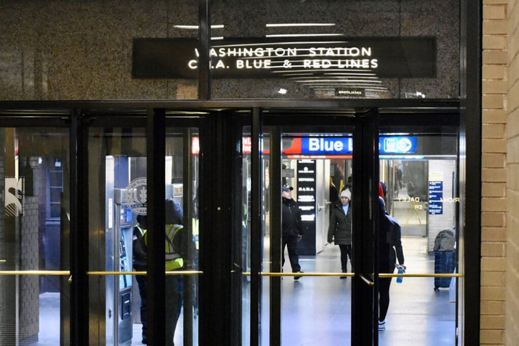 Color photograph of commuters entering a public-transit station through glass doors. Signage about the door reads "Washington Station C.T.A. Blue & Red Lines."