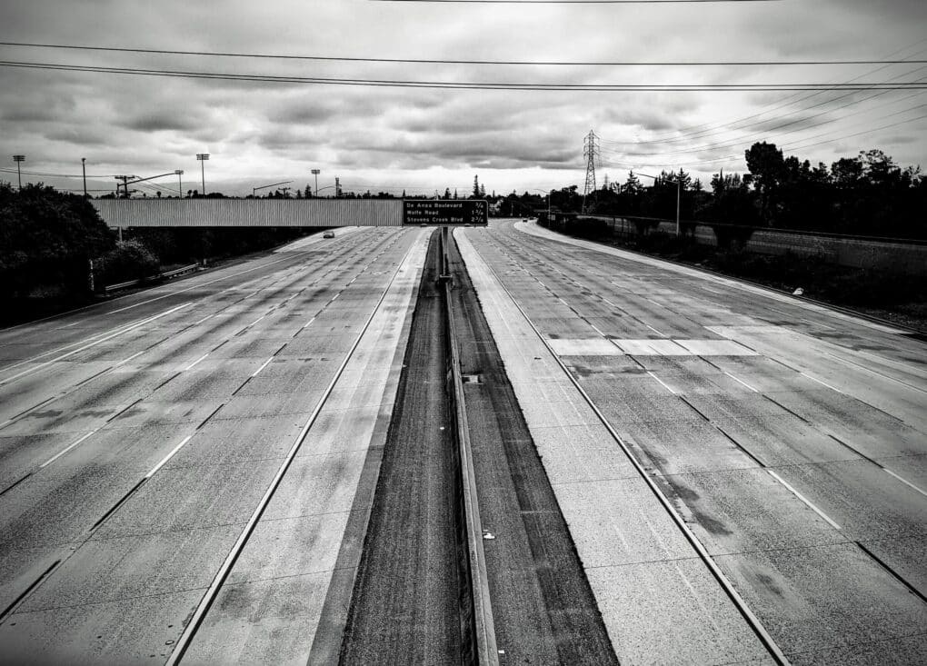 Broad view of all lanes of 8-lane highway, in black and white; there is one car in the distance but road is otherwise empty.