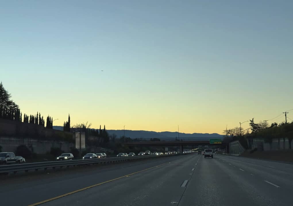 Twilight photo of highway taken from car perspective; road is empty though there is lots of traffic moving in opposite direction.