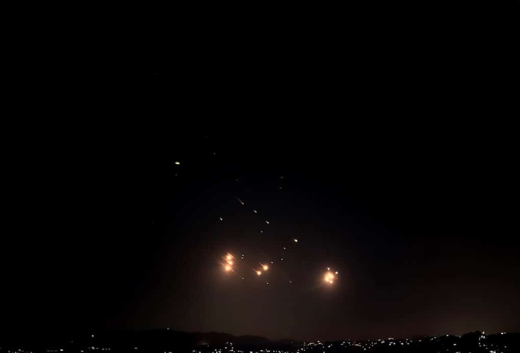Color photograph of black sky with cluster of very bright orange lights low in the sky at the horizon.