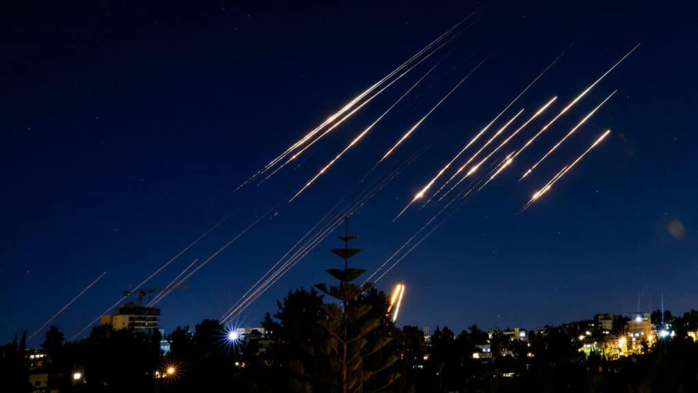 Color photograph of missiles in a dark sky, looking like streaks of golden light.
