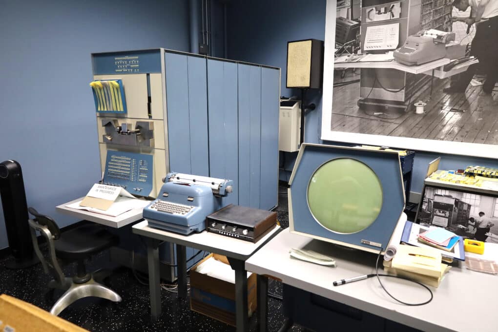 An image of antiquated office equipment. Three vintage desktop-size devices are on display. The color and materials suggest 1960s era. The center device is a typewriter but the other two are not recognizable.